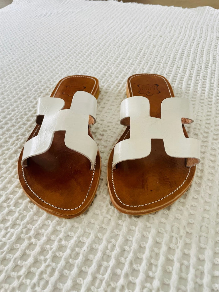 A pair of white leather slide sandals on white blanket from Moroccan Tribe.