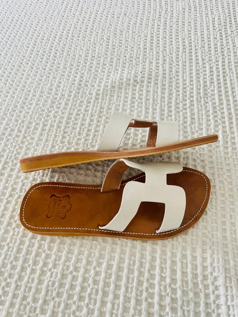 A pair of white leather slide sandals, on white blanket from Moroccan Rugs.